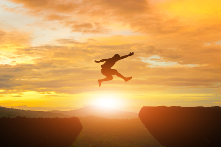 Men jump cliff sun light over silhouetteの写真素材