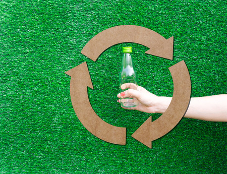 Hand hold show Recyclable plastic bottle a glass of water green background and paper cutterの写真素材