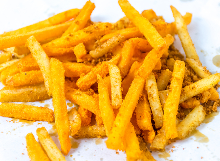 French fries In white paper wrap on wooden floor.