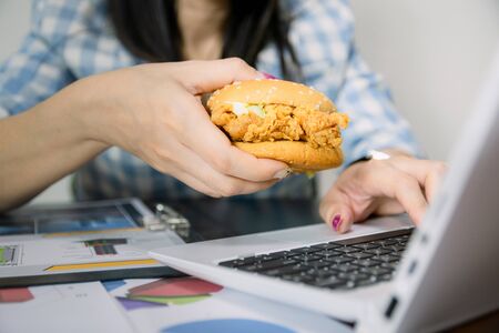 Women work and eat hamburgers to eat lunch in officeの写真素材
