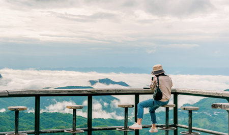 woman sitting on wooden balcony looking at mountain and fog view travelの写真素材