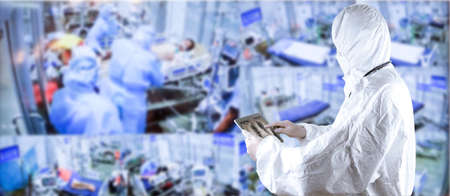 Doctors in the protective suits and masks holding a tablet are examining the infected patient in the control areaの写真素材
