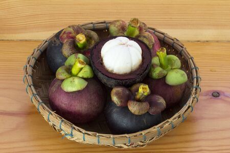 Ripe mangosteens (Garcinia mangostana) with green leaves in a basket on the wooden table, mangosteen queen.の写真素材