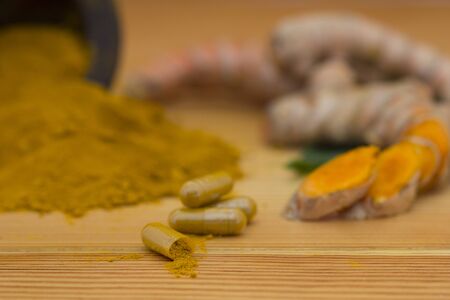 Turmeric (curcumin) powder and raw organic turmeric roots with capsule on wooden background,...