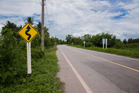 Road sign curved reminds the motorists and vehicles while driving with yellow sign reflecting light to be visible at night at the roadway in countryside of Thailandの写真素材