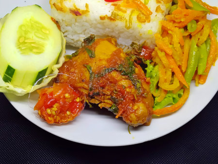 Fried chicken with rice and vegetables on a white plate on a black backgroundの写真素材