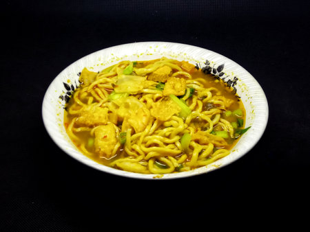 Noodles with chicken and vegetables in a white bowl on a black backgroundの写真素材