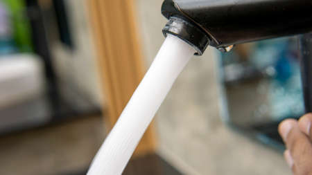 Jet streams of water running from a modern black faucet in the wash basin of outdoor swimming pool...