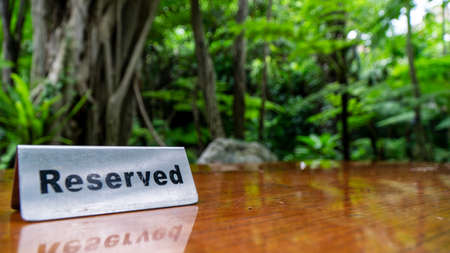 Reserved sign made out stainless steel plate on a laminated wooden table of a restaurant with trees and forest in the background.の写真素材