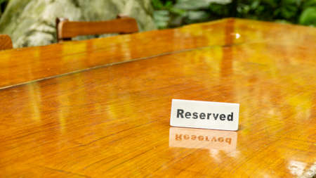 Reserved sign made out stainless steel plate on a laminated wooden table of a restaurant with trees and forest in the background.の写真素材