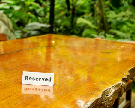 Reserved sign made out stainless steel plate on a laminated wooden table of a restaurant with trees and forest in the background.の写真素材