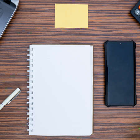 An office table working environment. Notepad, sticky note, pen plant, calculator and a lap top on a...
