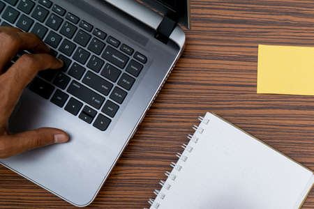 Typing on a keyboard while working on a project. A lap top, a mobile, calculator and plant are also on display on this brown striped working table.の写真素材