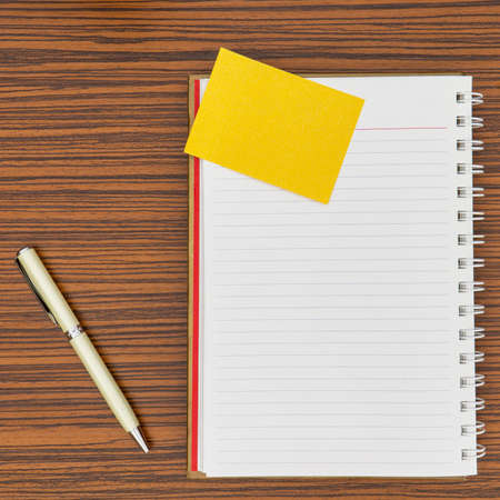 Personal notepad, yellow paper note and a pen on a zebra wood brown striped table.の写真素材