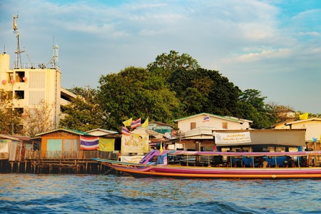 Bangkok, Thailand - December 8, 2015: People travelling by express boat in Chao Phraya river, Bangkok, Thailand. Old Thai traditional houses, village riverfront.のeditorial素材