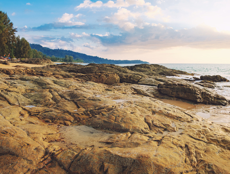 Beautiful seascape with sea and rock in Nang Thong Beach, Khao Lak, Thailand. View of bright blue sea with protruding stones in the foreground and crowded beach with bathing and walking peopleの写真素材