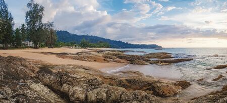 Coast of the Andaman sea at colorful sunset, Nang Thong Beach, Khao Lak, Thailand. Beach sunset is a cloudy sunset sky with a wave rolling to shore and crowded beach with bathing and walking peopleの写真素材