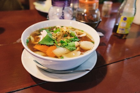 Hot and spicy Thai Dishes. Blurred image of a savoury thick soup made with squid rings, spices and vegetables and crushed peanuts on cafe background. Selective focusの写真素材