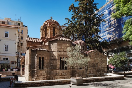 Athens, Greece - September 22, 2017: Church of Panaghia Kapnikarea is a greek orthodox church with Byzantine frescoes in the center of famous Ermou Street. Young man looks at phone sitting on parapetのeditorial素材