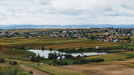 A typical natural landscape in the country of Suceava: fields, a small lake and a village of houses with red roofs, mountains on the horizon, Romania. Panoramic view.の写真素材