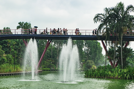 Singapore, Singapore - January 16, 2018: View of bridge with walking tourists in the Gardens by the Bay after rain, Singapore. Fountains next to the ticket office.のeditorial素材