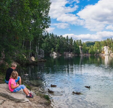 Adrspach, Czech Republic - August 16, 2018: Mother and daughter feeding ducks on lake in rock city Adrspach, National park of Adrspach, Czech Republicのeditorial素材