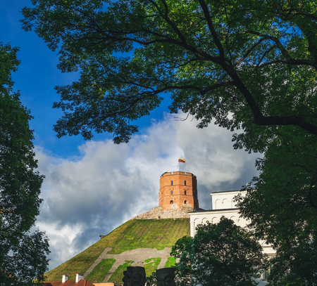 Gediminas tower with flag on hill in a beautiful summer day in Vilnius, Lithuania. Down side view of the tower among the tree branchesのeditorial素材