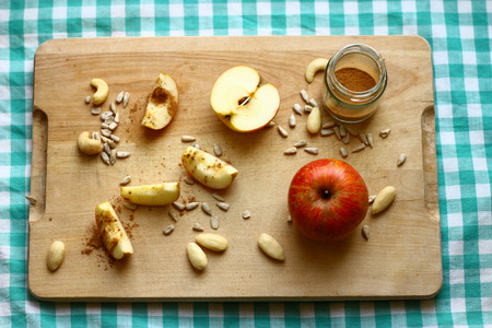 Healthy breakfast or snack - pieces of red organic apple, almonds, cashew nuts and sunflower seeds on wood and green tableclothの写真素材