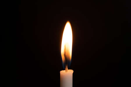 A candle lit by fire illuminates the darkness.