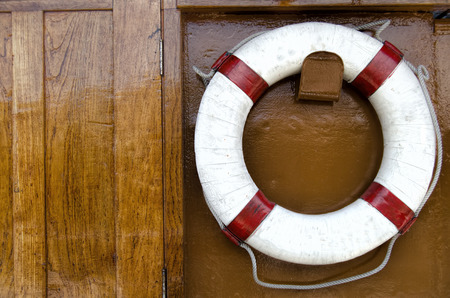 Red lifebuoy with rope on weathered wooden wall in port