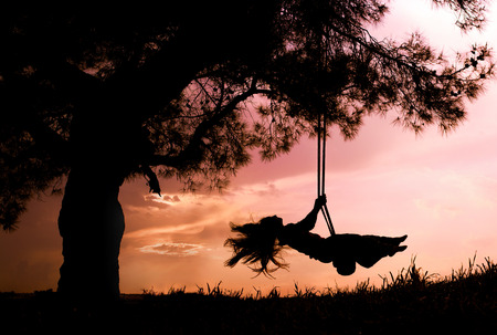 silhouette of happy young woman on a swing with sunset backgroundの写真素材