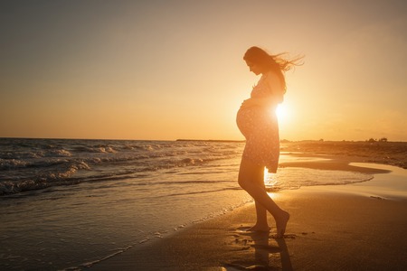 silhouette of a pregnant woman walking on the beach at sunsetの写真素材