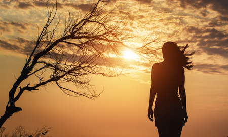 Silhouette of lonely woman standing under a tree.の写真素材