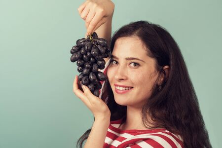 Smiling girl holding grapes near her face and smiling broadly to the viewer.