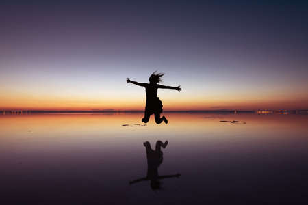 Woman jumping up in a beautiful sunset w,th reflection.の写真素材