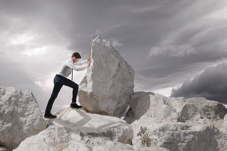 Business concept, Young businessman pushing large stone uphill with copy space.の写真素材