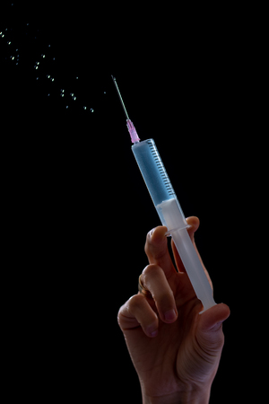 Syringe with a medicine in a female hands, isolated on black.の写真素材