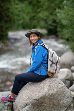 Smiling hiker girl with white backpack sitting on a rockの写真素材