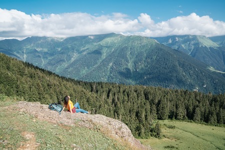 Young happy woman with backpack standing on a rock looking to a valley below.の写真素材