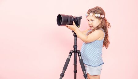 Little girl holding camera and smiling on pink background.の写真素材
