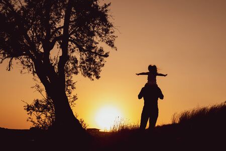 Happy father and daughter silhouette standing on against sunset timeの写真素材
