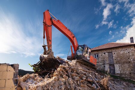 A heavy industrial work machine, digger is destroying an abandoned old building.