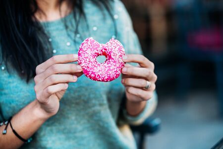 Woman is eating a delicious and colored donut.の写真素材