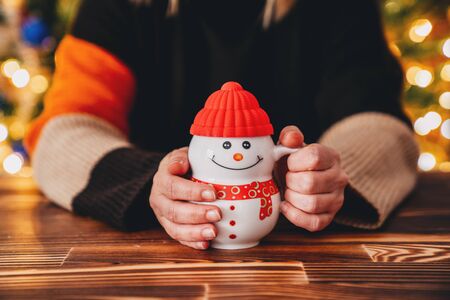 Young woman is sitting in a cafe and drink with a snowman cup. Christmas concept.の写真素材