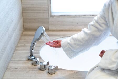 Woman is checking temperature touching running water with hand for having a bath.