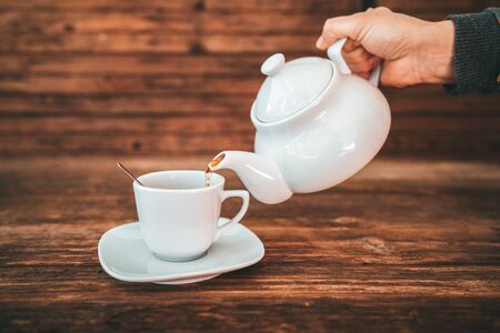 Tea time, brewing and pouring tea, cup of freshly brewed tea, warm soft and light, with wooden background.の写真素材