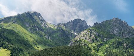 Panoramic view of row of mountains and forest with a blue sky and coudsの写真素材