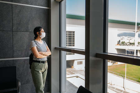 Young woman is standing in a waiting hall with a protection mask. Corona virus outbreaking. High...