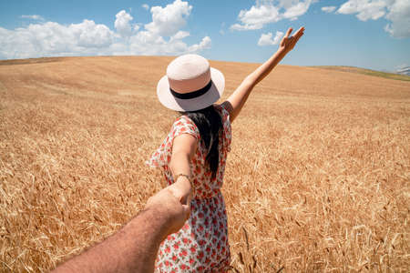 Beautiful woman holding hand in a agriculture field with blue sky and clouds background. Romance and rural concept. High quality photoの写真素材