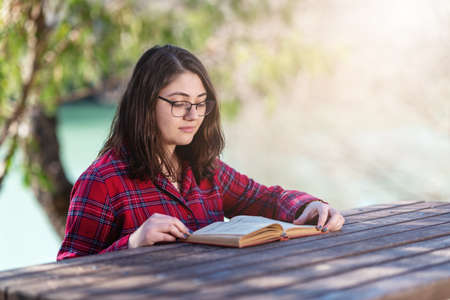 Intellectual young girl sitting and reading book or stuydying with books in a park. High quality...